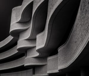 Vista en contrapicado de un edificio brutalista con balcones curvos de concreto y textura de piedra, en una imagen en blanco y negro.