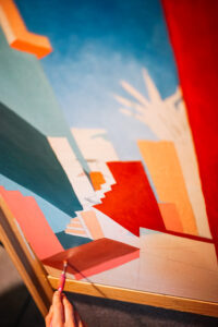 Mano pintando un cuadro abstracto con formas geométricas en tonos rojos, azules y naranjas.