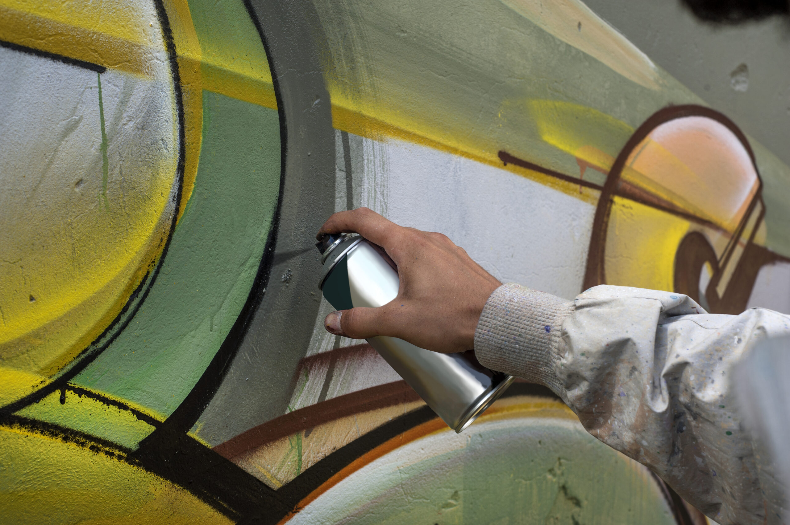 Mano de un artista callejero pintando un mural colorido con aerosol sobre una pared de hormigón.
