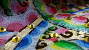 Primer plano de un patrón decorativo multicolor con formas curvas y lentejuelas doradas sobre superficie texturada.