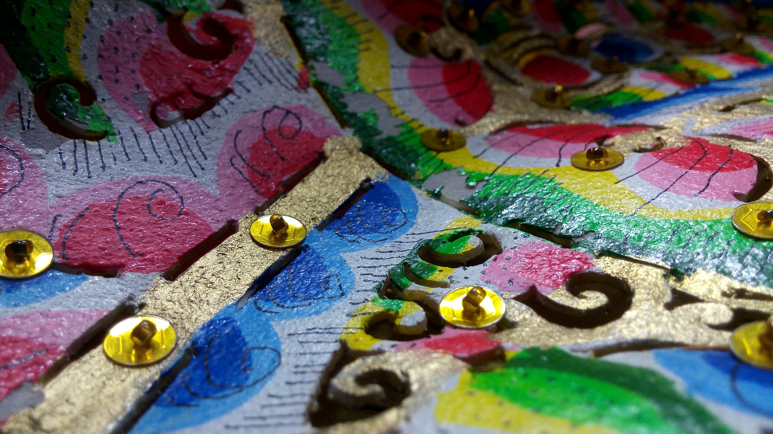 Primer plano de un patrón decorativo multicolor con formas curvas y lentejuelas doradas sobre superficie texturada.