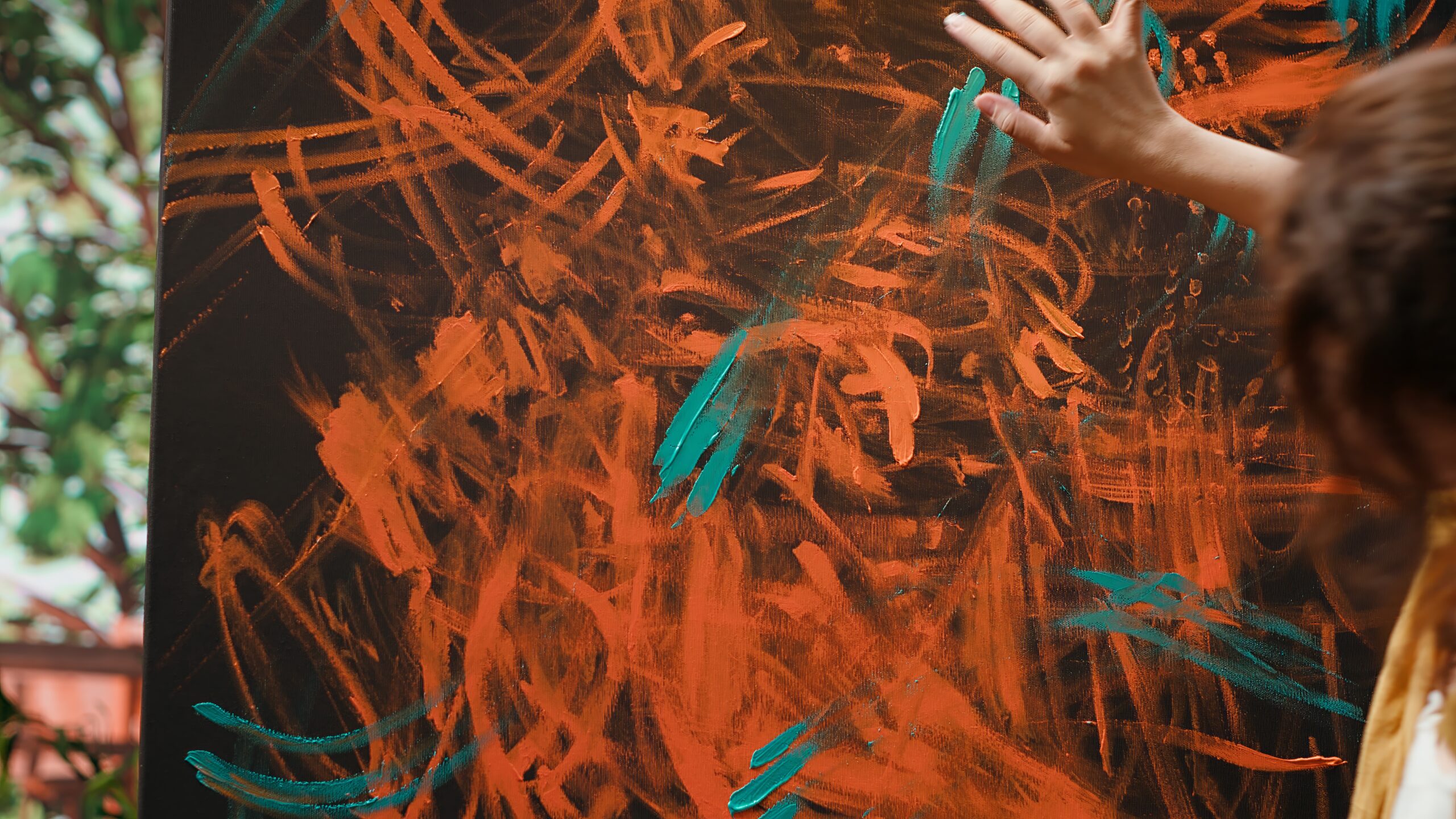Mano de artista pintando con los dedos sobre lienzo con trazos abstractos en naranja y turquesa