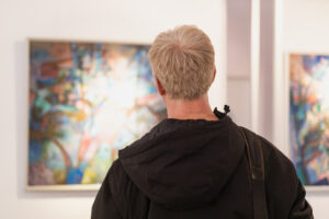 Hombre de espaldas observando una pintura abstracta en una galería de arte.