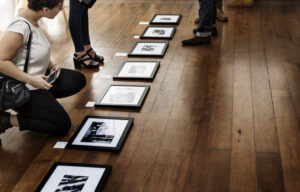 Persona observando fotografías en una exposición de arte mientras otra persona está de pie al fondo.