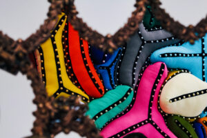 Decoraciones textiles de colores brillantes con tachuelas metálicas, observadas a través de un marco ornamentado.